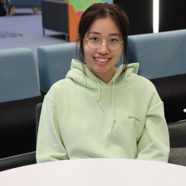 Student in green hoodie sat at desk.